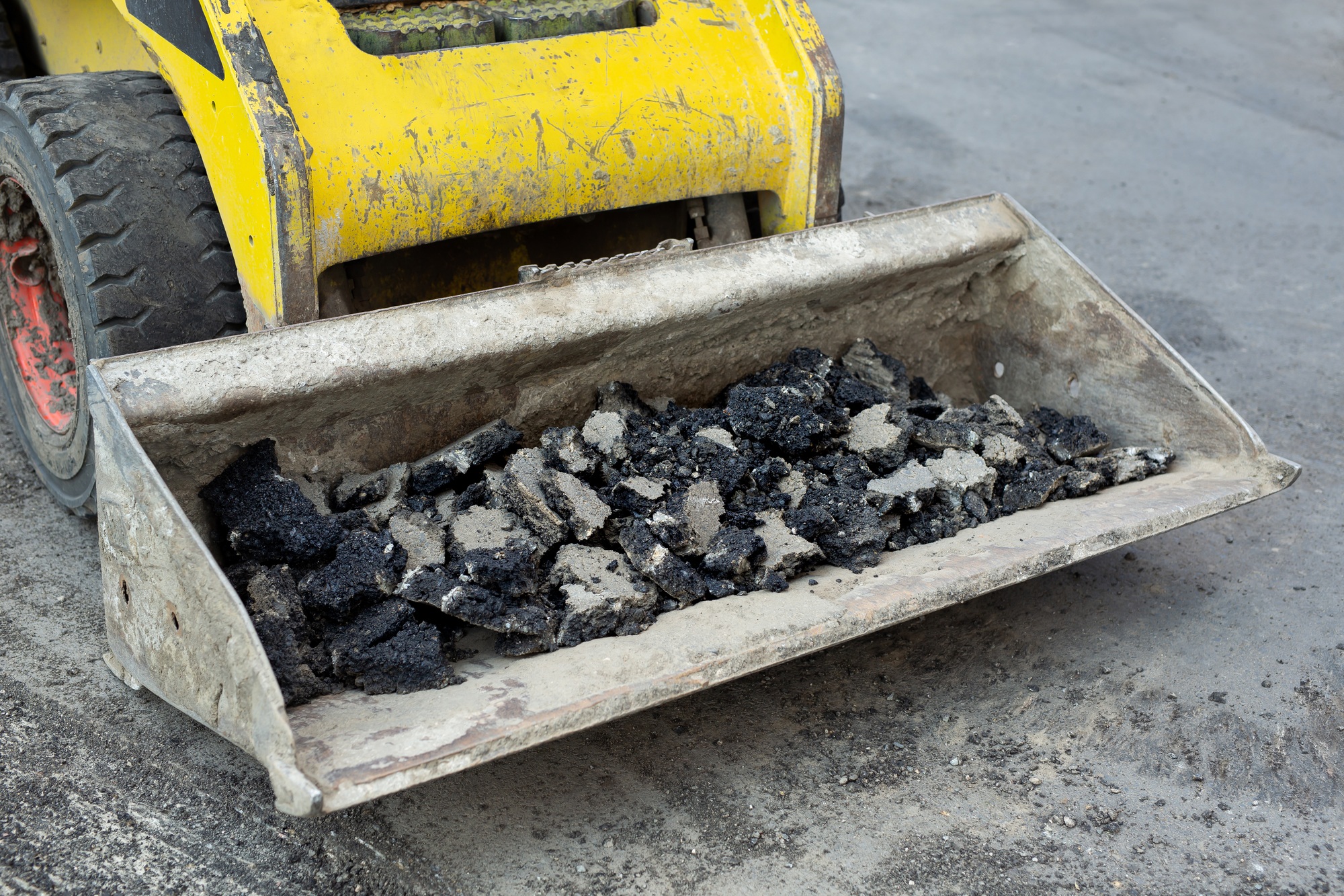 Tractor bucket with old asphalt. Road repair works.
